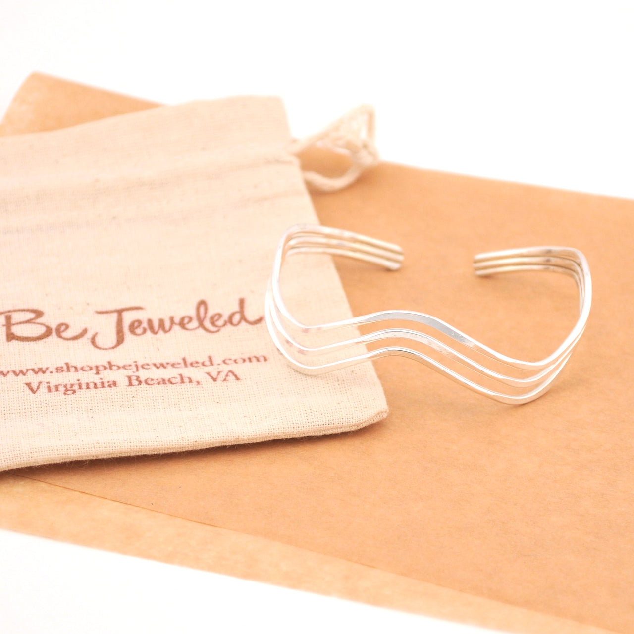 Silver bracelet on a beige cloth with 'Be Jeweled' branded pouch