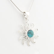 A silver sunburst pendant necklace featuring a round turquoise stone in the center, suspended from a delicate silver chain against a plain white background.