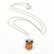 Silver owl pendant necklace with amber-colored stone on a white background
