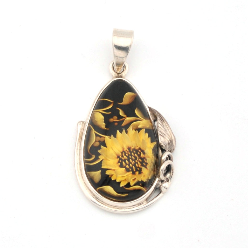 Teardrop-shaped pendant with sunflower design on a black background, set against a white background.