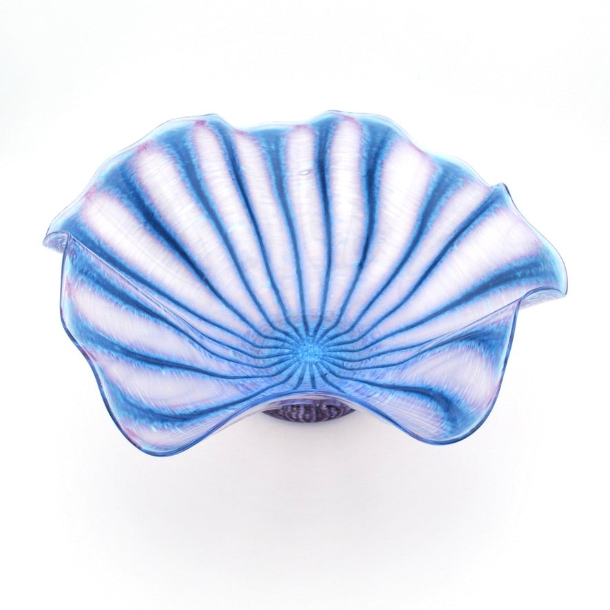 A scallop-shaped glass bowl with a blue and white striped pattern, photographed from a top-down angle on a white background.