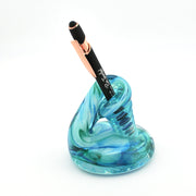 Blue glass pen holder with a black and rose gold pen on a white background