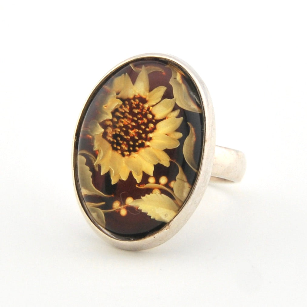 Silver ring with a sunflower design on an oval stone against a white background