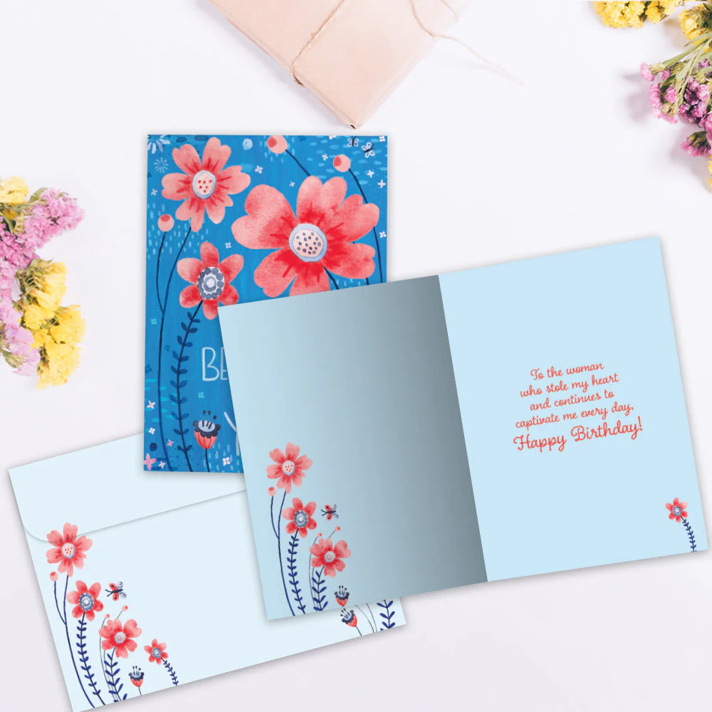 Floral birthday card with a blue background and pink flowers on a white surface.