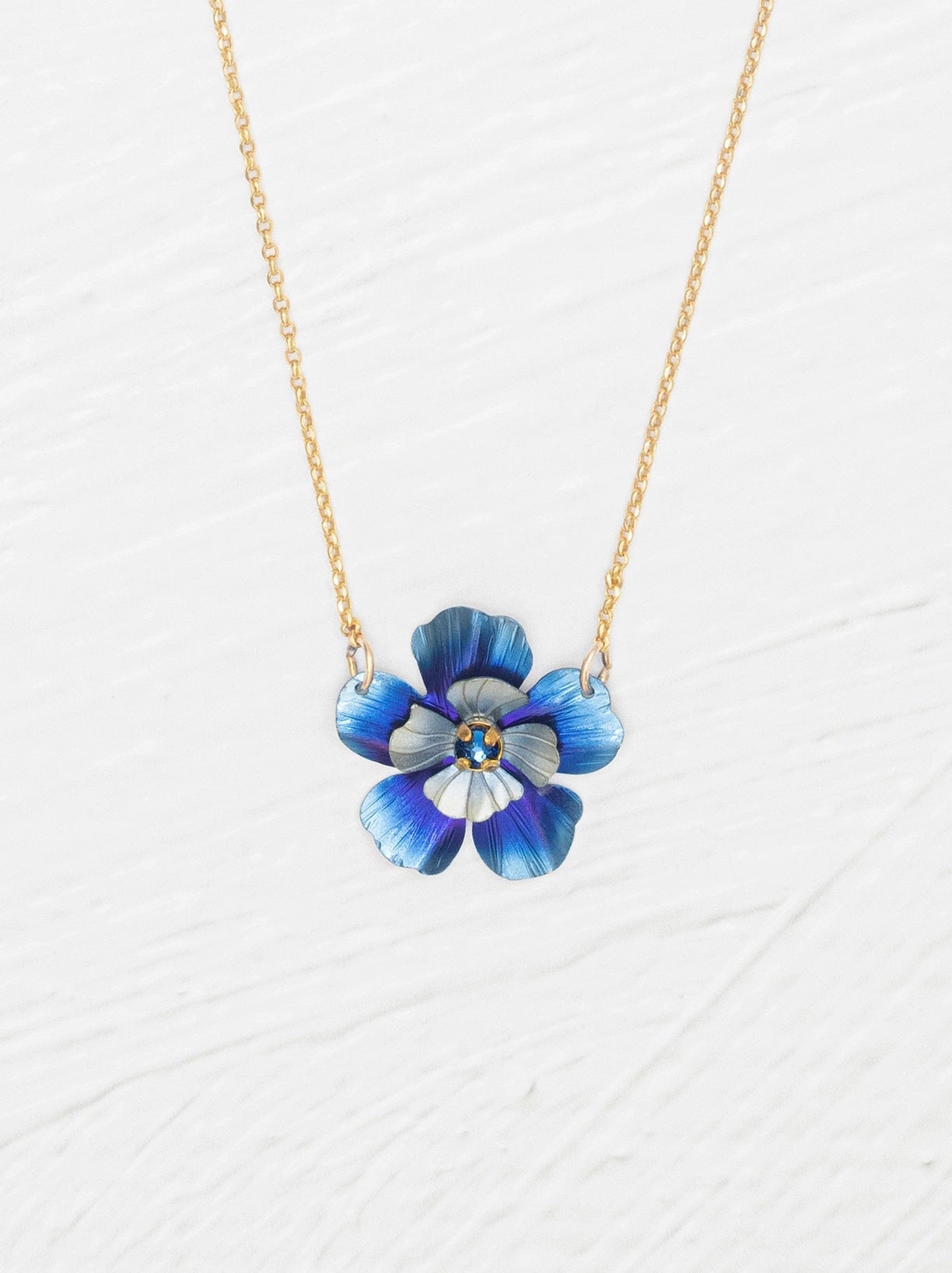 Blue flower-shaped pendant on a gold chain against a white background