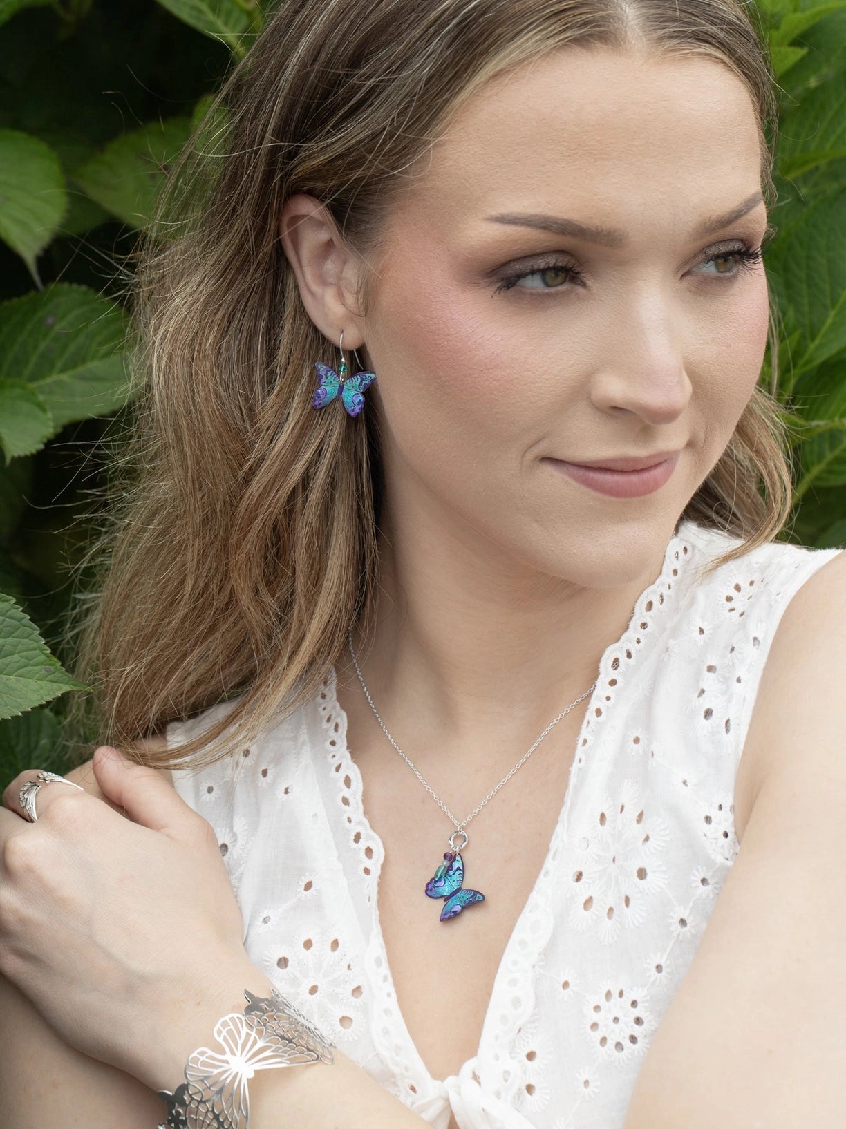 Woman wearing a butterfly necklace and earrings with a green leafy background