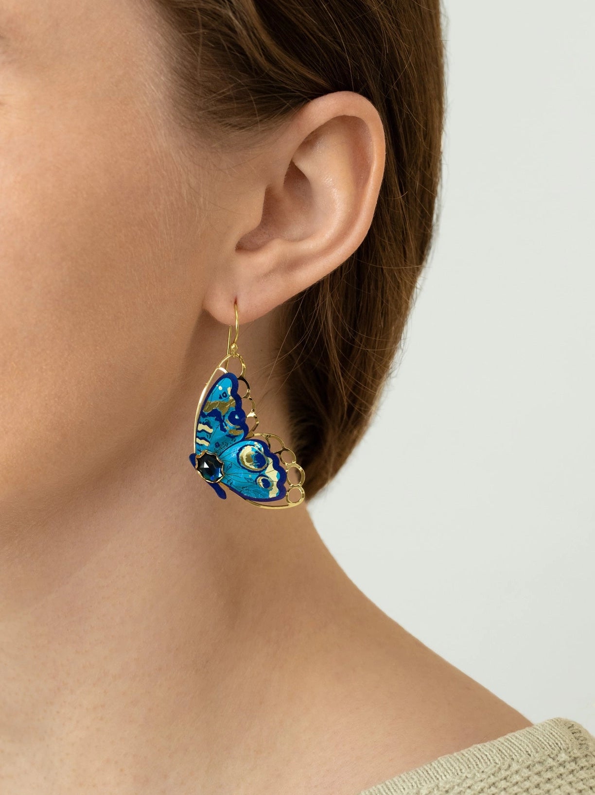Blue butterfly earring worn by a person on a white background