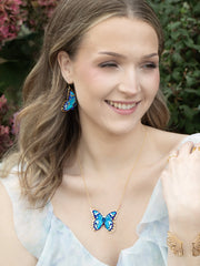Woman wearing butterfly-themed jewelry outdoors with greenery in the background