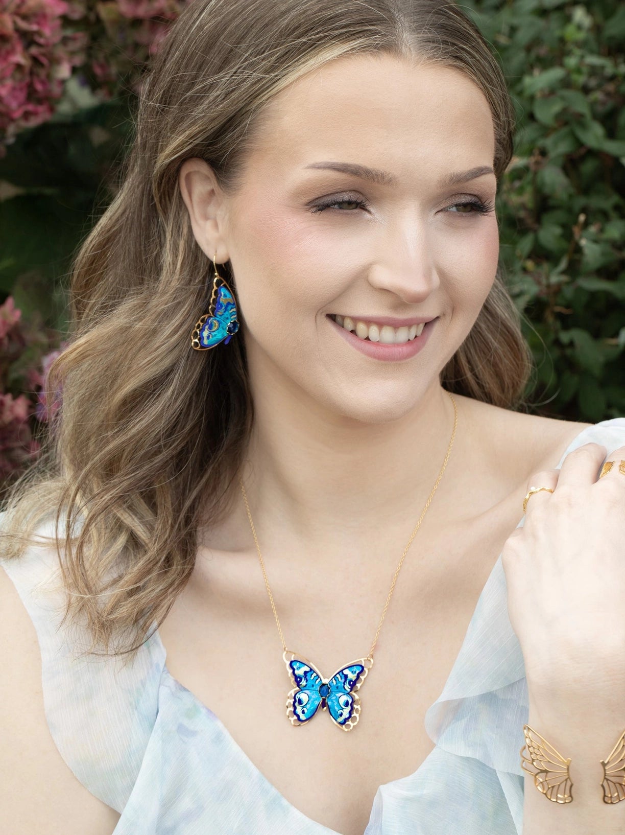 Woman wearing butterfly-themed jewelry outdoors with greenery in the background