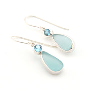 Pair of earrings with light blue teardrop stones and silver hooks on a white background