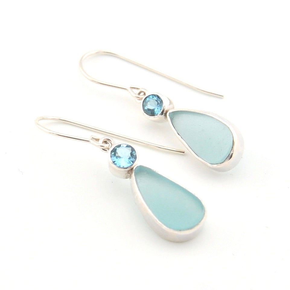 Pair of earrings with light blue teardrop stones and silver hooks on a white background