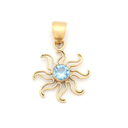 A gold sunburst pendant featuring a central round light blue gemstone, shown against a plain white background.