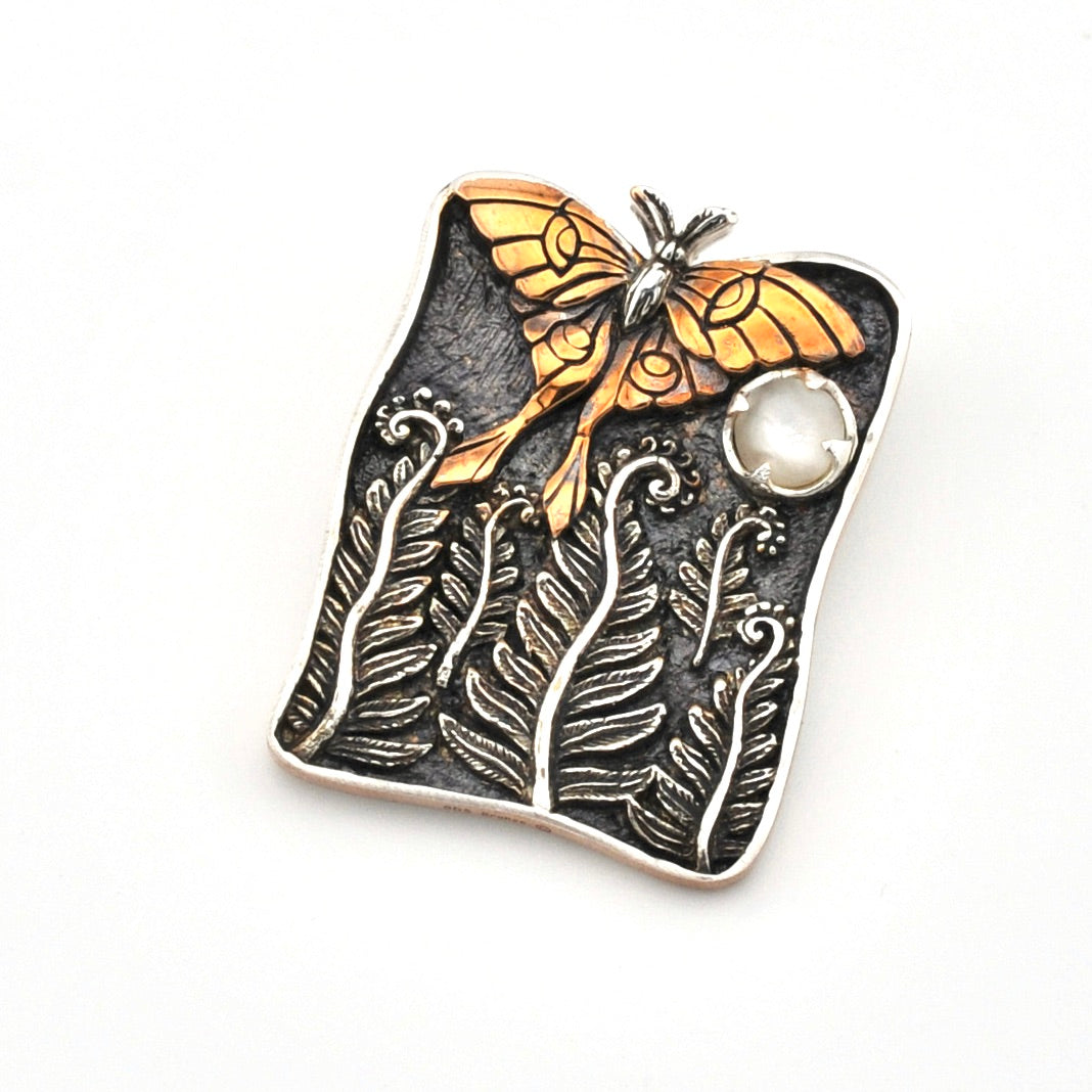 Decorative pendant with luna moth and leaf design on a white background