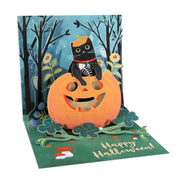 A 3D pop-up Halloween greeting card featuring a black cat wearing a witch hat sitting on a jack-o'-lantern, with a spooky forest background and 'Happy Halloween!' written on the green base.