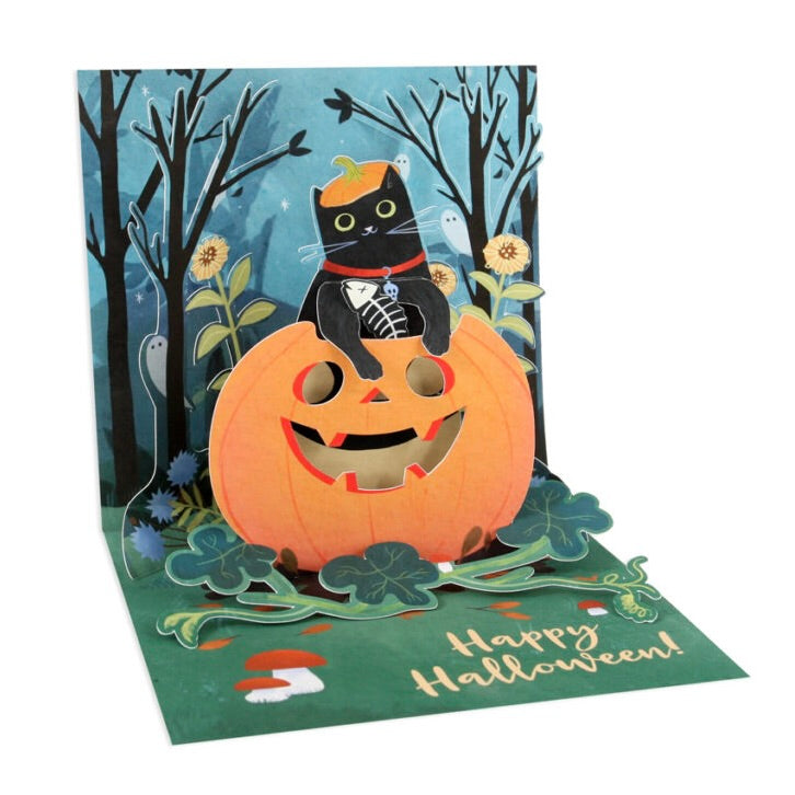 A 3D pop-up Halloween greeting card featuring a black cat wearing a witch hat sitting on a jack-o'-lantern, with a spooky forest background and 'Happy Halloween!' written on the green base.