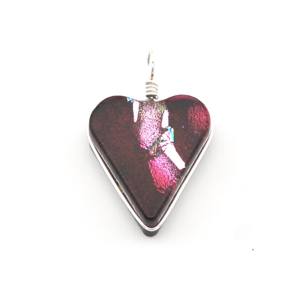 A heart-shaped glass pendant with a dark red and magenta iridescent center, bordered by a silver metal frame and topped with a silver wire loop, shown on a plain white background.