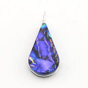 A teardrop-shaped pendant featuring a vibrant blue and purple iridescent dichroic glass set in a silver bezel with a silver wire-wrapped bail, shown on a plain white background.