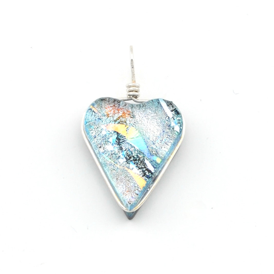 A heart-shaped glass pendant with a silver wire-wrapped setting, featuring a multicolored fusing pattern of light blue, yellow, orange, and black on a white background.