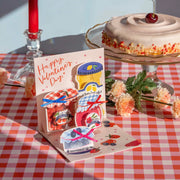 Valentine's Day card with ice cream illustrations on a checkered tablecloth with a cake and flowers.