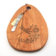 Wooden cutting board with engraved dragonfly and floral design, accompanied by a cheese knife on a white background.