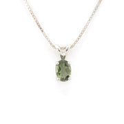 A silver pendant necklace featuring an oval-cut green gemstone in a four-prong setting, suspended from a delicate silver chain against a plain white background.