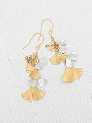 A pair of gold and silver dangling earrings with a fan-shaped leaf design, displayed on a light gray textured background.