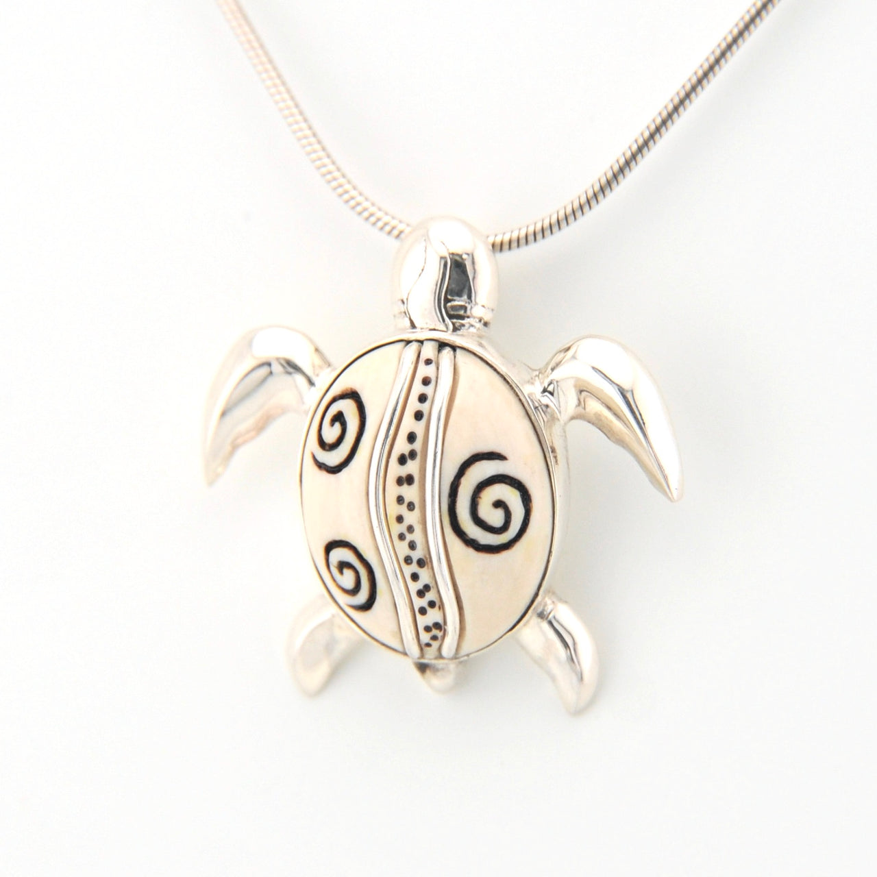 Silver turtle pendant with spiral patterns on a white background