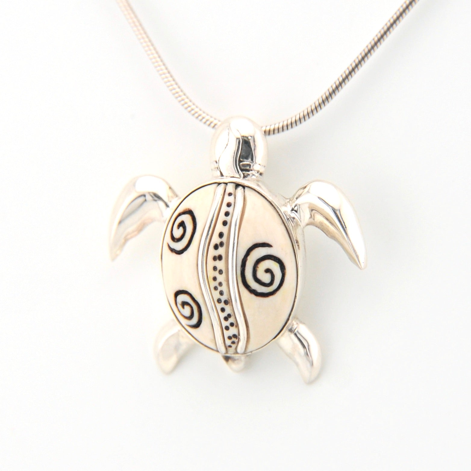 Silver turtle pendant with spiral patterns on a white background