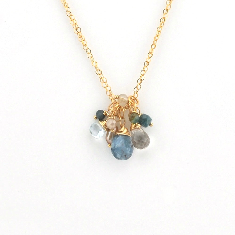 A gold chain necklace with a delicate cluster pendant featuring multiple small gemstones in blue, green, gray, and beige, displayed on a clean white background.