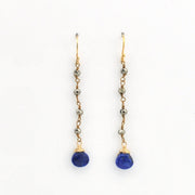 A pair of gold drop earrings with small metallic beads and a deep blue teardrop-shaped gemstone at the bottom, shown on a plain white background.