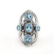 A silver-toned ring featuring five light blue gemstones in an ornate filigree design, set against a plain white background.