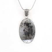 An oval pendant necklace featuring a black-and-white marbled stone with dendritic crystal patterns, set in a silver-toned bezel and suspended from a silver chain.