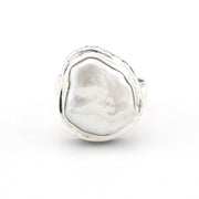 A sterling silver ring featuring a large, irregularly shaped white baroque pearl bezel-set in a textured, hand-drawn style silver frame, shown on a plain white background.