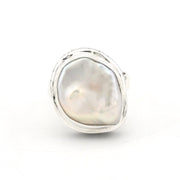 A sterling silver ring featuring a large, irregular baroque pearl with iridescent white and soft pinkish-gold tones, set in a polished bezel-style silver frame against a plain white background.