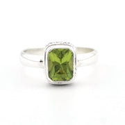 A silver ring featuring a rectangular green peridot gemstone in a bezel setting, shown on a plain white background.