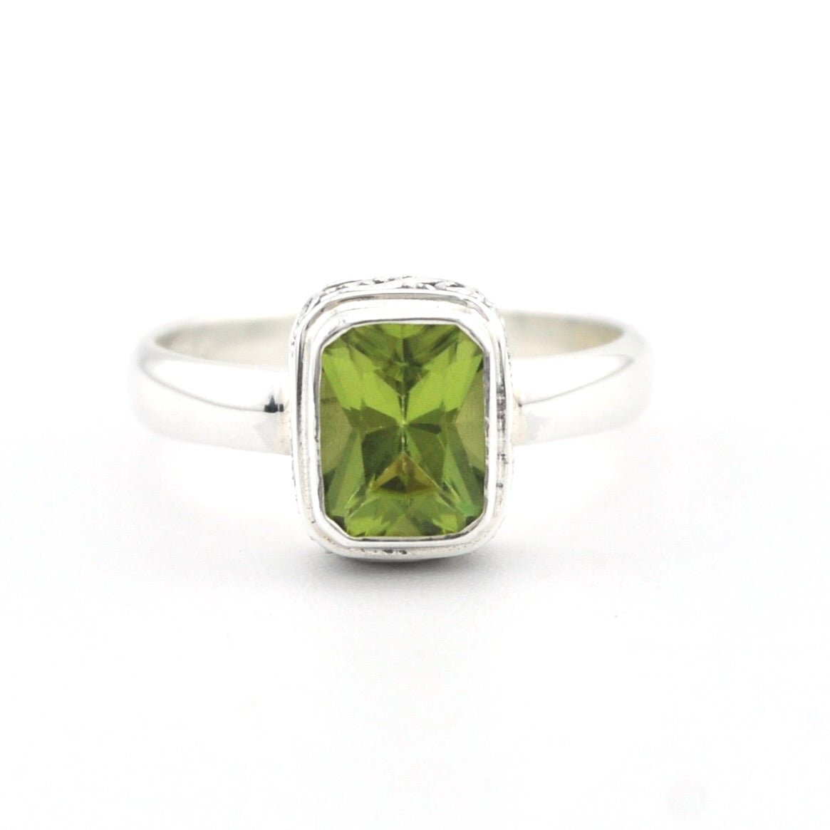 A silver ring featuring a rectangular green peridot gemstone in a bezel setting, shown on a plain white background.