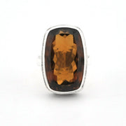 A silver ring featuring a large, cushion-cut faceted brown gemstone, shown against a plain white background.