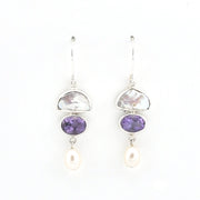 A pair of silver drop earrings featuring a polished white stone, a purple amethyst oval, and a dangling white pearl on a clean white background.