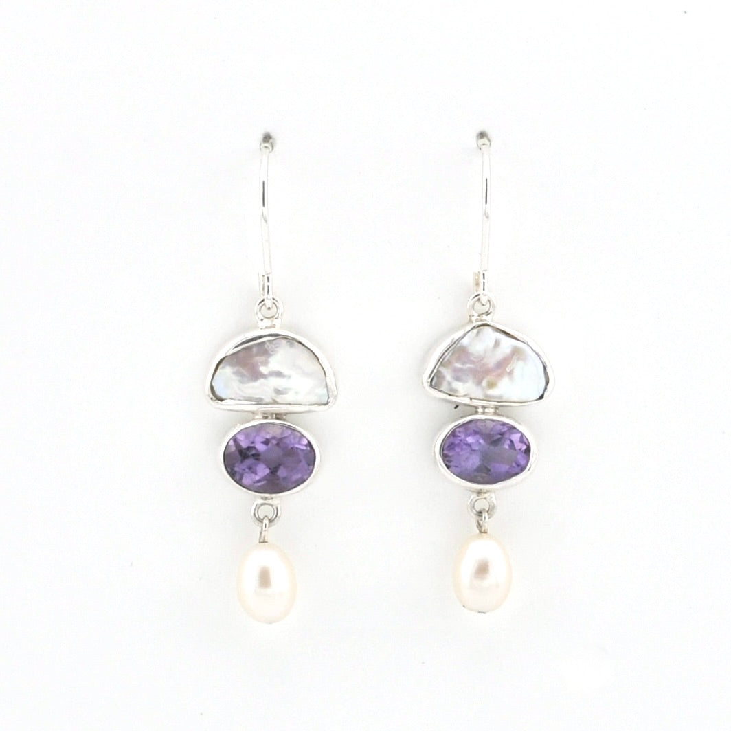 A pair of silver drop earrings featuring a polished white stone, a purple amethyst oval, and a dangling white pearl on a clean white background.