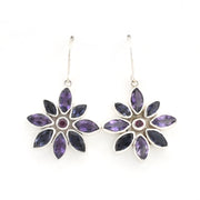 A pair of silver dangle earrings featuring a flower design with marquise-cut purple gemstones and a small round purple center stone, shown on a plain white background.