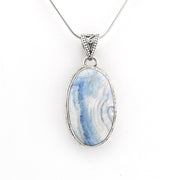 An oval pendant necklace featuring a blue and white marbled stone in a silver bezel setting, suspended from a silver chain against a plain white background.