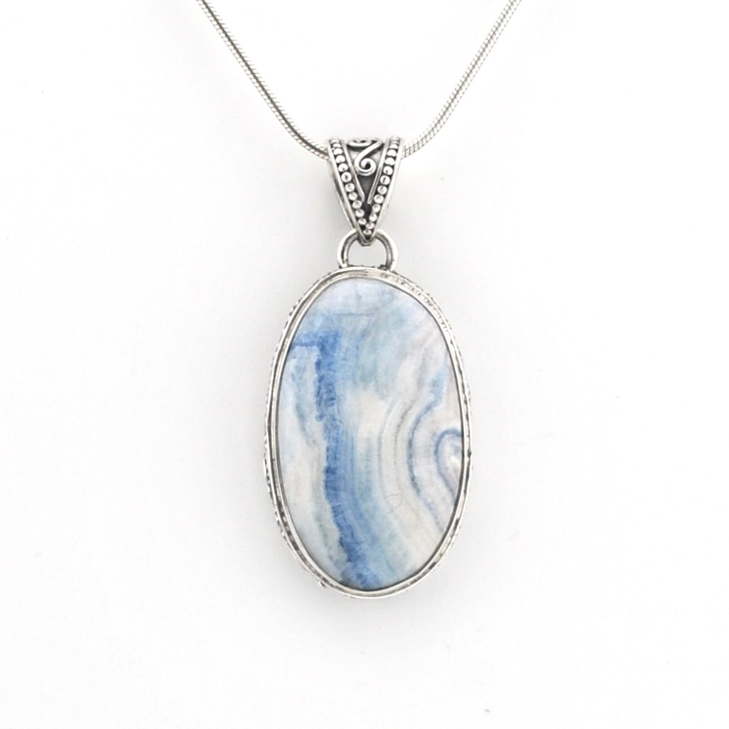 An oval pendant necklace featuring a blue and white marbled stone in a silver bezel setting, suspended from a silver chain against a plain white background.