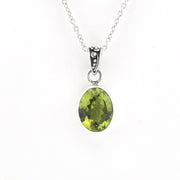 A silver pendant necklace featuring an oval-cut green gemstone in a bezel setting, suspended from a delicate silver chain against a plain white background.