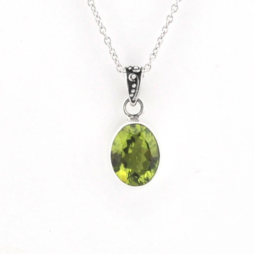 A silver pendant necklace featuring an oval-cut green gemstone in a bezel setting, suspended from a delicate silver chain against a plain white background.