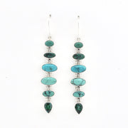 A pair of long drop earrings featuring a vertical stack of oval and teardrop-shaped turquoise stones in green and blue tones, set in silver-tone metal with small clear spacer beads, on a plain white background.