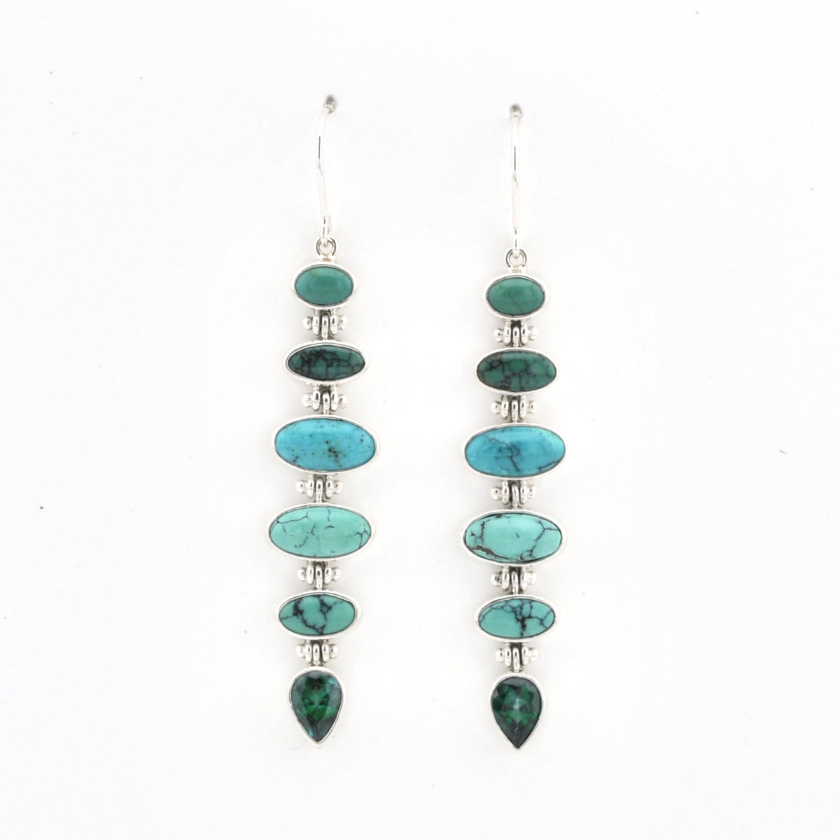 A pair of long drop earrings featuring a vertical stack of oval and teardrop-shaped turquoise stones in green and blue tones, set in silver-tone metal with small clear spacer beads, on a plain white background.