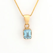 Gold necklace with a blue gemstone pendant on a white background