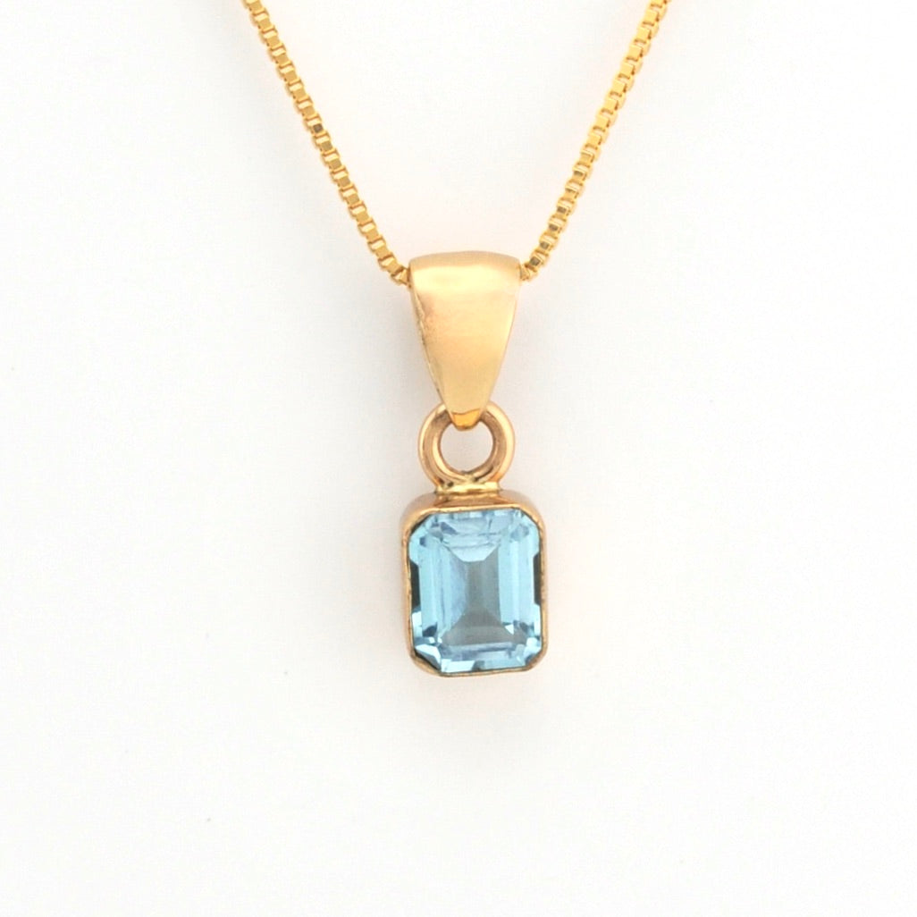 Gold necklace with a blue gemstone pendant on a white background