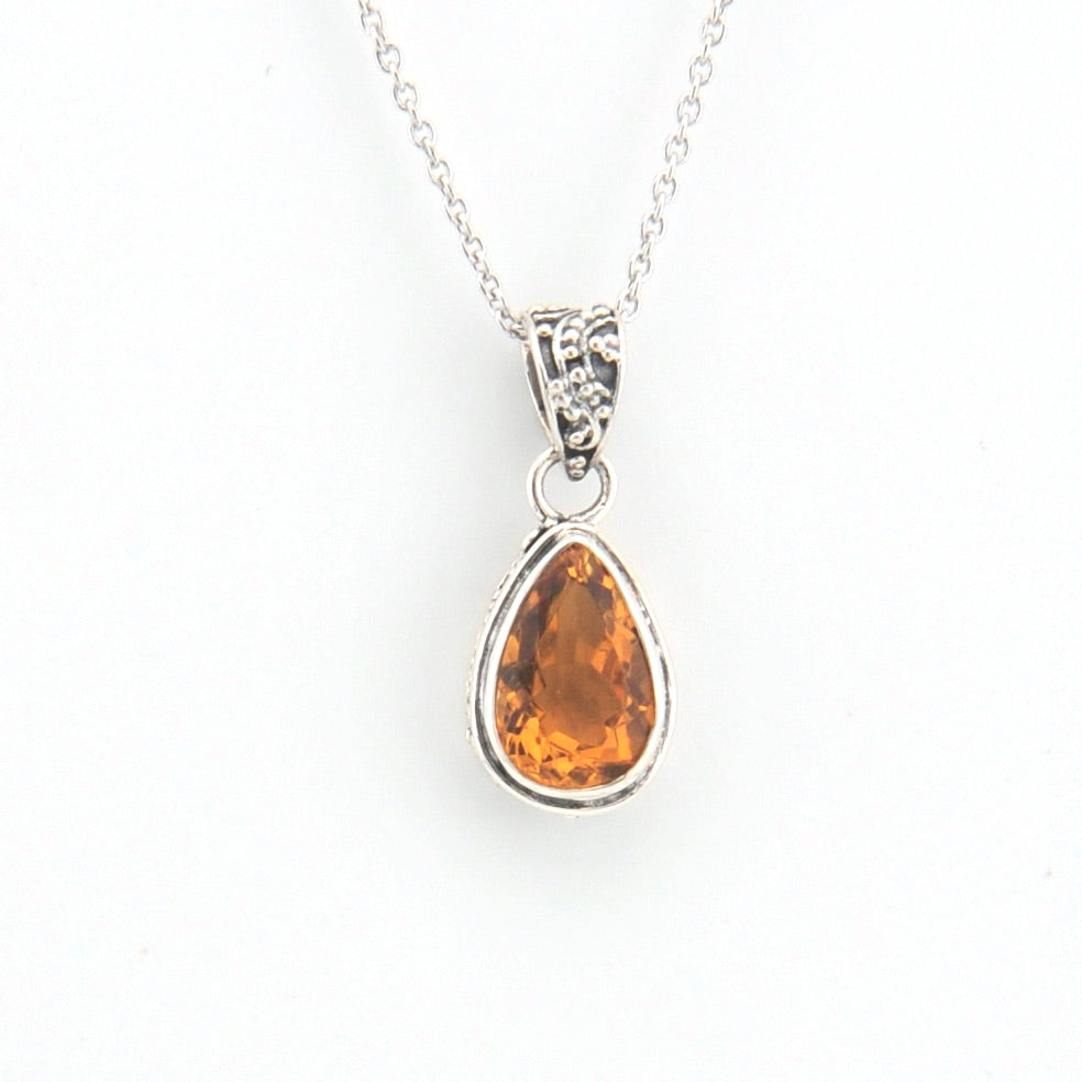 Teardrop-shaped citrine pendant on a silver chain against a white background