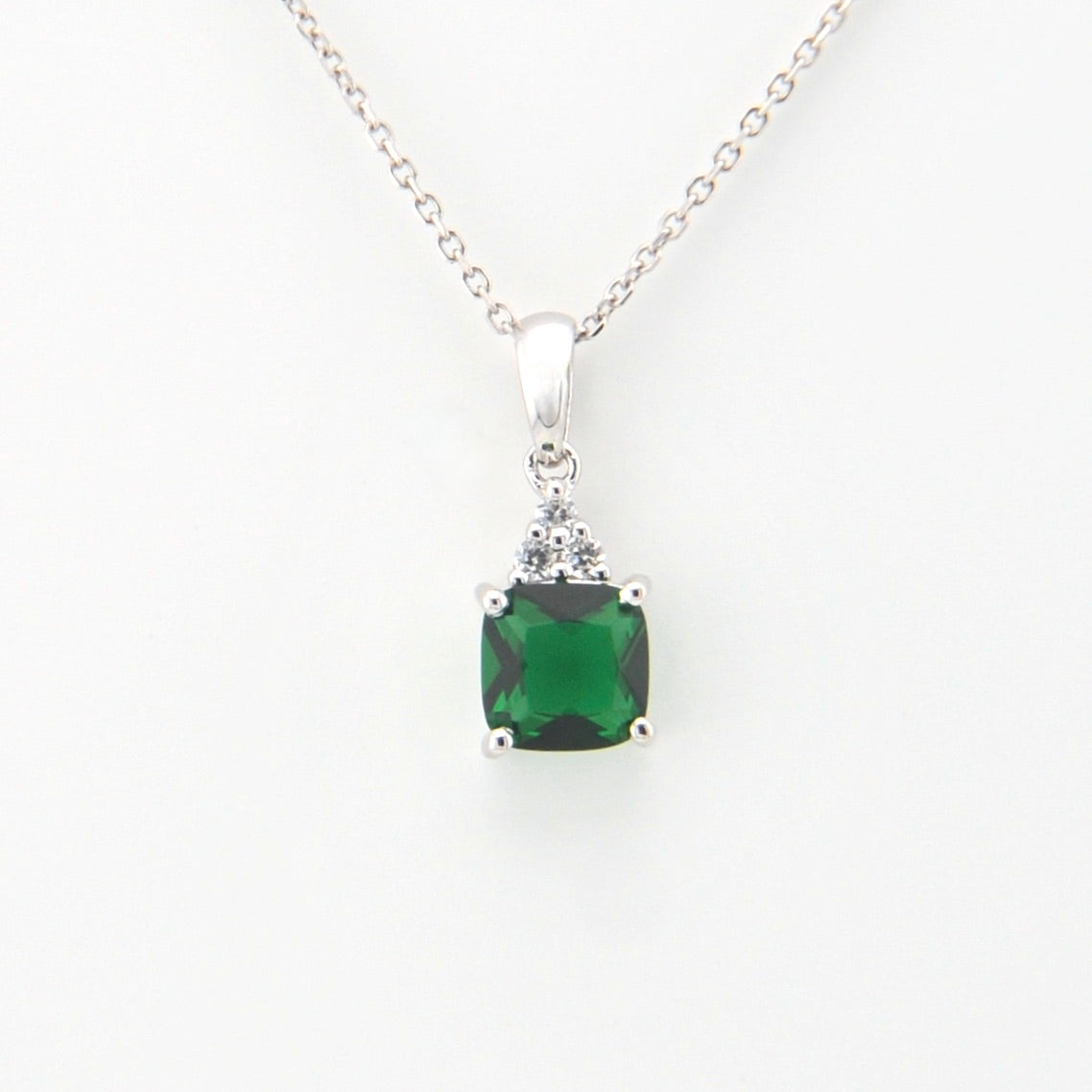 Green gemstone pendant on a silver chain against a white background